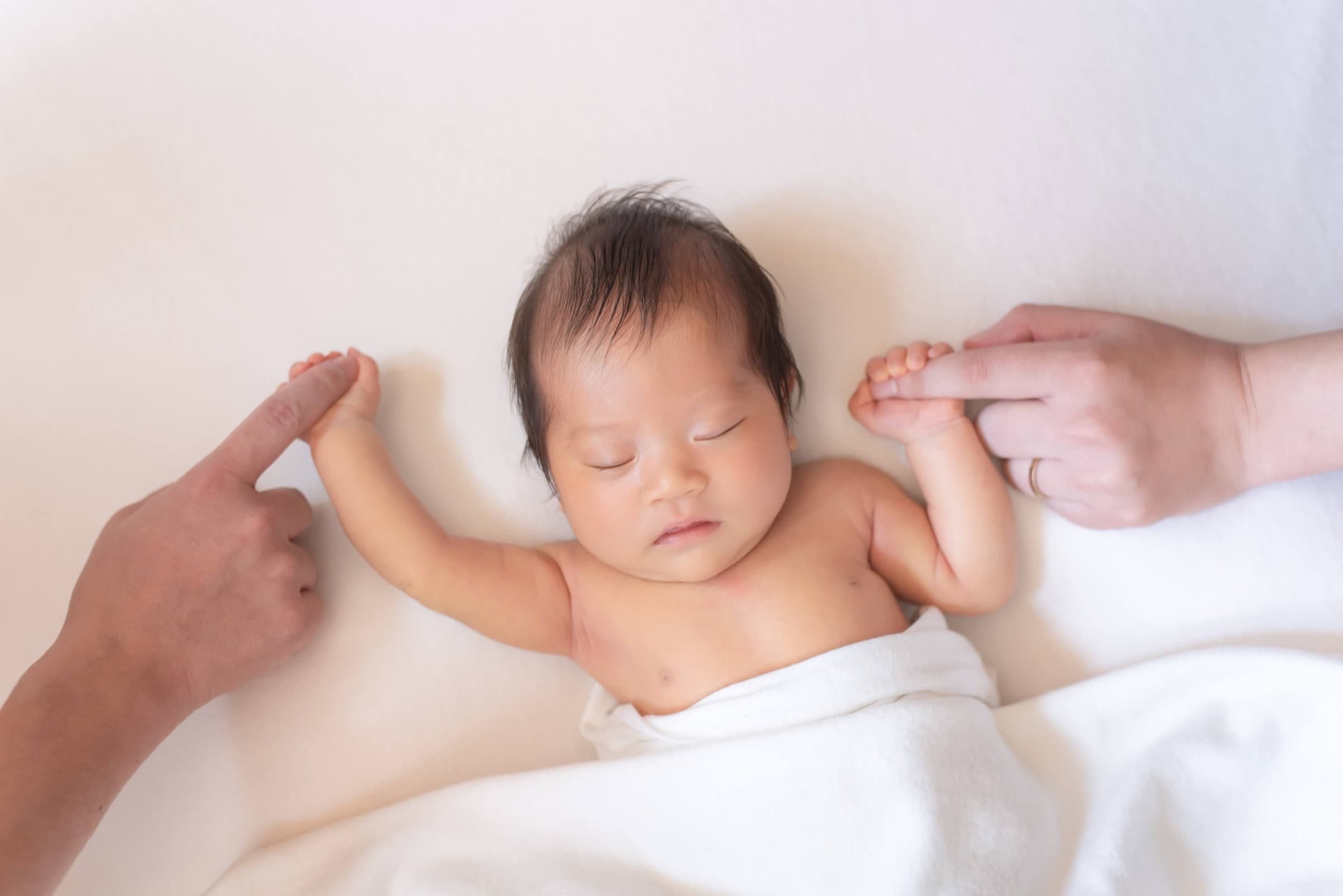 新生児を両親の手で包むニューボーンフォト